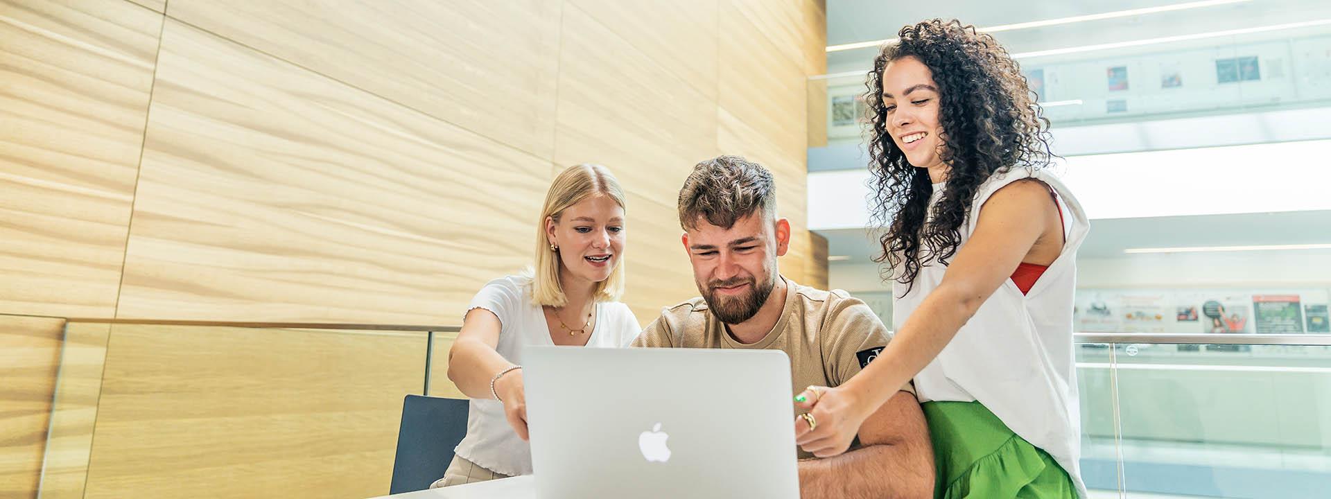 Drei Studierende mit Laptop Auf dem Foto sind drei Studierende zu sehen, die zusammen in einen Laptop schauen.