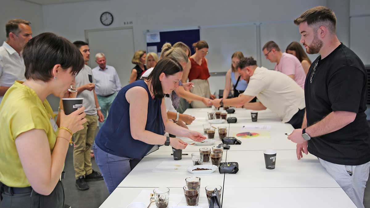 Beim Kaffeeworkshop verkosten verschiedene Teilnehmer*innen unterschiedliche Kaffeesorten mit einem Probierlöffel. Ganz vorne links steht Kursleiterin Antonia Hagen-Kettemann und zeigt wie der Kaffee zur Verkostung geschlürft werden muss.