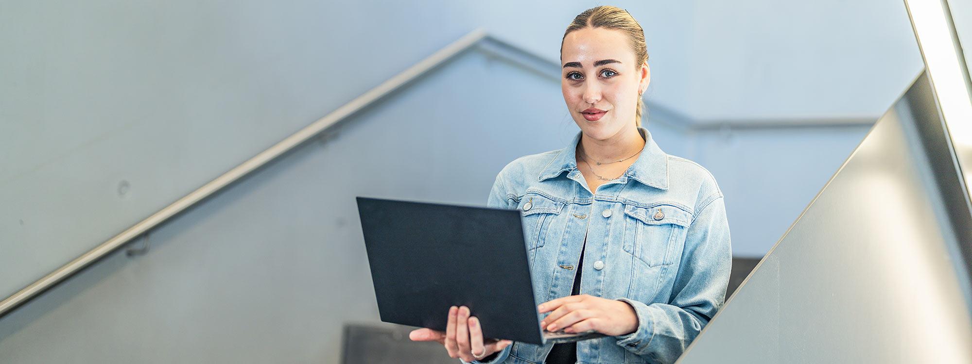 Frau mit Laptop auf einer Treppe Auf dem Foto ist eine Frau zu sehen, die auf einer Treppe steht und einen aufgeklappten Laptop in der Hand hält.