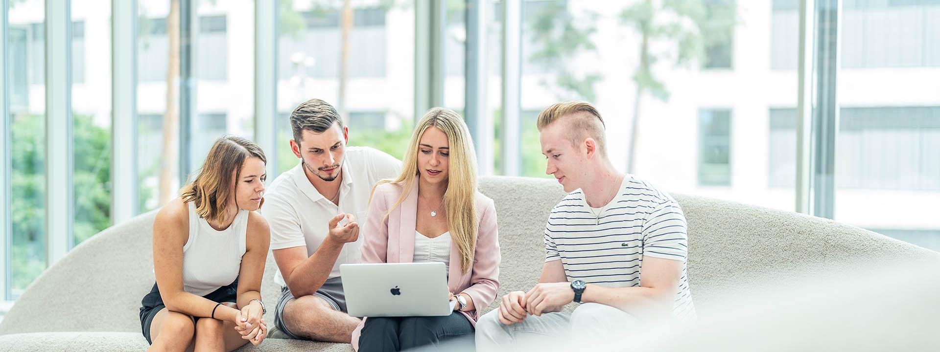 Vier Personen mit Laptop Auf dem Foto sind vier Studierende zu sehen, die nebeneinander sitzen und in einen Laptop schauen.